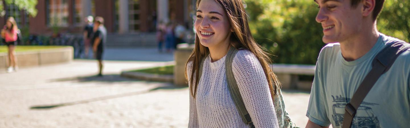 Female and male students smiling and walking outside on campus