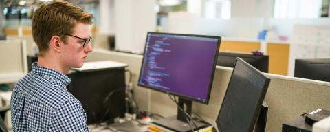 Male student sitting at desk working on computer programming