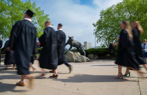 UNH graduates walking by Wildcat statue 