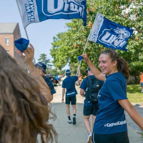 Students walking in the summer holding UNH flags