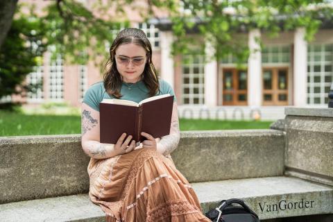 Student reading a book in the front of the UNH Library